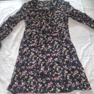 Svart blommig långärmad klänning - Supersöt svart klänning från Gina Tricot med blommigt mönster i rosa, gul och grå. Långärmad och med mjuk, stretchig passform som sitter bekvämt. Perfekt för dig som gillar romantiska vibes och vill ha något som sticker ut lite extra.