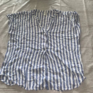 Randig vit och blå skjorta med v-ringning - Säljer en luftig skjorta med v-ringning och korta ärmar. Skjortan har ett fräscht randigt mönster i vitt och blått, perfekt för varma dagar. Materialet känns lätt och svalt, och passformen är avslappnad. Perfekt för dig som gillar en chill och stilren look.