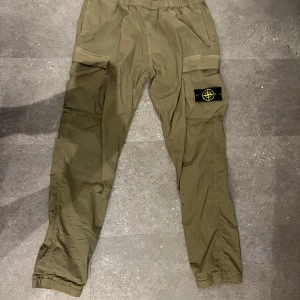 Stone Island cargopants i olivgrönt - Säljer ett par olivgröna cargopants från Stone Island med klassisk patch på benet. Byxorna har elastisk midja med snörning, stora fickor på sidorna och är tillverkade i bomull. Perfekta för en streetwear-look.