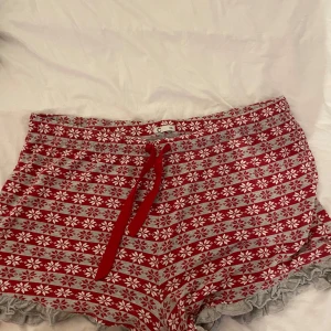 Röda mönstrade shorts med snörning - Supermysiga röda shorts med vitt snöflingemönster och grå volangkant. De har en bekväm hög midja och röd snörning framtill. Perfekta för chill dagar hemma eller när du vill ha något extra cozy under vintern.