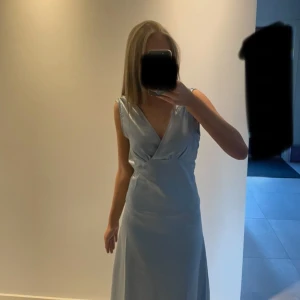 Ljusblå balklänning med v-ringning - Säljer en elegant ljusblå balklänning i satinliknande material. Klänningen har v-ringad fram och bak, är ärmlös och har en mjukt figurnära passform. Tyget har en fin glans och faller snyggt längs kroppen. Perfekt för dig som vill ha en stilren och chic look. Även öppen rygg. Använd endast en gång på balen men lite skitig längst ner men inget man tänker på.
