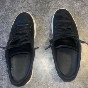 Svarta sneakers från Selected Homme - Svarta sneakers från Selected Homme med vit sula och klassisk rund tå. Skorna har snörning och är tillverkade i skinn med textilfoder. Perfekt för dig som gillar stilrena och enkla sneakers med en clean look.