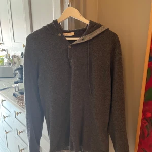 luca faloni kashmir hoodie - Exklusiv mörkgrå hoodie från Luca Faloni i mjuk kashmir. Tröjan har huva med knappar och snörning, samt långärmad passform. Använd ett få tal gånger och är som ny. Kommer med originalpåse och box. Nypris 4000kr