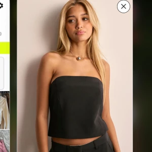 Svart axelbandslös tubtopp - Stilren svart tubtopp med rak skärning och croppad passform. Toppen är axelbandslös och har en enkel, minimalistisk look som passar perfekt till både jeans och kostymbyxor. Materialet ser ut att vara mjukt och lätt, vilket ger en snygg siluett. Lappen kvar