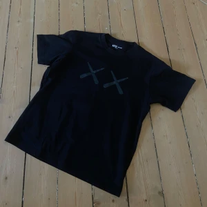 Uniqlo x KAWS | T-shirt - Unik T-shirt från exklusivt samarbete mellan Uniqlo, KAWS och Andy Warhol. Stilren svart design med KAWS “XX” på bröstet och ikoniskt porträtt av Warhol på ryggen. Herrstorlek S – normal i passform. 100 % bomull. I mycket gott skick, endast sparsamt använd.  Perfekt för dig som gillar konst, design och streetwear. 