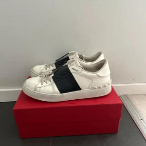 Valentino garvani  - Snygga vita valentino garvani sneakers med svarta detaljer. Skorna har en rund tå och snörning. Samt de ikoniska nitarna på  sidorna. Perfekt för en stilren look i hyfsat bra skick.😉💕