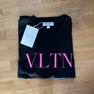 Svart Valentino t-shirt - Säljer en svart t-shirt från Valentino med stort rosa VLTN-tryck på bröstet. Orginal förpackning och lapp medföljer. Klassisk rund hals och korta ärmar. Perfekt statement-plagg för dig som gillar exklusiva märken och stilren design. 