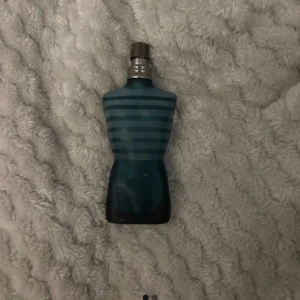 Le Male herrparfym från Jean Paul Gaultier - Ikonisk herrparfym i form av en blå manlig torso med horisontella ränder. Flaskan är tillverkad i glas och har en metallfärgad spraykork. Doften är känd för sin fräscha och kryddiga karaktär.