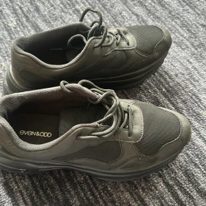 Svarta sneakers från Even&Odd - Säljer ett par svarta sneakers från Even&Odd. Skorna har snörning och är gjorda i en kombination av syntetmaterial och mesh för extra andningsförmåga. Perfekta för en stilren och sportig look.
