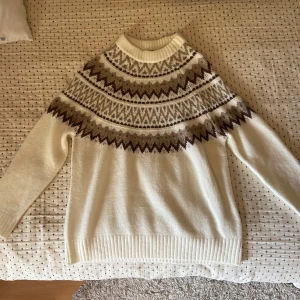 Vit stickad tröja med mönster - Supermysig vit stickad tröja från 157 med brunt och beige nordiskt mönster över axlar och bröst. Tröjan har lång ärm och ribbade muddar vid hals, ärmslut och nederkant. Tröjan har aldrig använts och är i mycket bra skick.