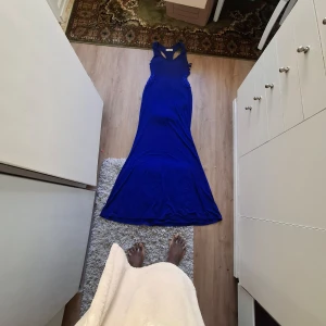 Kornblå långklänning med v-ringning - Säljer en kornblå långklänning med v-ringning och breda axelband. Klänningen har en figurnära passform upptill och är utsvängd nertill. Snygga detaljer i form av mesh och små paljetter vid midjan. Perfekt för dig som vill sticka ut.