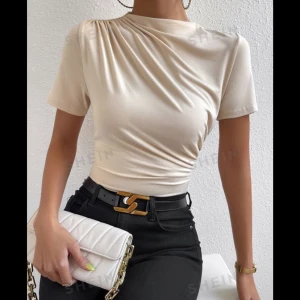 Beige croppad topp med drapering från SHEIN - Trendig beige croppad topp från SHEIN med korta ärmar och snygg drapering vid axeln. Toppens material är mjukt och stretchigt, perfekt till svarta jeans eller kjol. Rund halsringning och figurnära passform.
