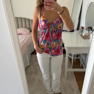 Färgglad blommig linnetopp med knyt - Säljer en färgglad linnetopp med blommigt mönster i rosa, rött, gult och blått. Toppen har smala axelband och en söt knytdetalj framtill. Perfekt för varma dagar och somriga outfits!