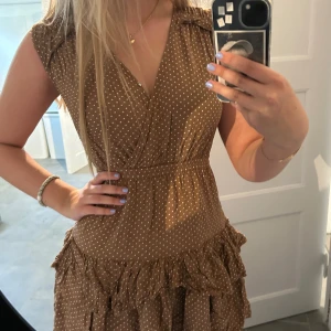 Prickig klänning med volanger från Designers Remix Girls - Skön söt prickig klänning från designers remix girls!! Klänningen har storleken ”14 år” och kan knäppas vid bysten. V ringning, brun med vita prickar, kortärmad och volangdetaljer. Passar bra till nästan alla årstider!! Säljer då den är för liten (klänningen är ostruken på bilderna) DENNA ANNONS ÄR ÅTERPUBLICERAD💕