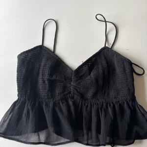 Svart topp med öppen rygg, volanger och smala axelband - Super söt svart kort topp med volang, öppenrygg och smala axelband🖤🖤🖤