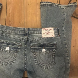 True Religion Joey Low Rise Flare Jeans - Säljer ett par klassiska blå jeans från True Religion, modell Joey Low Rise Flare. Jeansen har en snygg tvätt och  ikoniska bakfickor med silverfärgade knappar. Perfekt för dig som gillar en lite utsvängd passform och låg midja. På sista bilden kan man se att jag sprätt upp sömmarna längst ner för att göra dem lite längre. Jag har endast använd dem en gång!💕