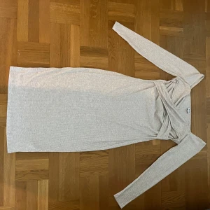 Ljus ribbad långärmad klänning - Säljer en ljus, ribbad klänning med lång ärm och omlottdetalj upptill. Klänningen är figurnära och har en enkel, stilren design som passar perfekt till många tillfällen.
