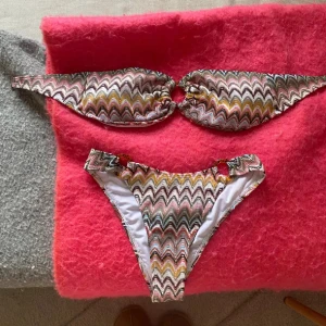 Flerfärgad bikini med missonimönster - Säljer en snygg bikini med färgglatt missoni i gult, rosa  och brunt. Överdelen har bandeau-modell och underdelen sitter fint ibak🧡🧡 Köpt i spanien och passade inte mig så aldrig använd