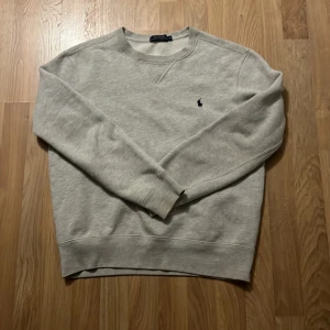 Ljusgrå sweatshirt från Polo Ralph Lauren - Säljer en ljusgrå sweatshirt från Polo Ralph Lauren med rund halsringning och liten broderad logga på bröstet. Tröjan har långa ärmar och ribbade muddar vid ärmslut och nederkant. Perfekt för en avslappnad stil.