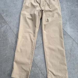 Beige sommarbyxor från NN07  - Säljer ett par beige byxor från NN07, No Nationality. Byxorna har rak passform, elastisk midja med dragsko och stängs med dragkedja och knapp. Superfint skick.