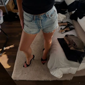 Ljusblå jeansshorts från Zara  - Säljer ett par ljusblå jeansshorts med fransig kant och slitna detaljer. Shortsen har hög midja, knappar framtill och klassiska fickor både fram och bak. Perfekta för sommaren och ger en avslappnad look.