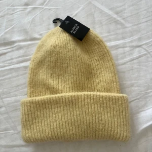 Gul ribbad mössa från Bik Bok - Säljer en mjuk, varm och super söt ljusgul mössa från BikBok i alpackaull. Mössan är ribbstickad med uppvikt kant och har en enkel, klassisk design som passar perfekt till kyliga dagar.