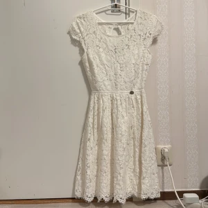 Studentklänning spets  - Superfin vit spetsklänning från Chiara Forthi med kort ärm och rund halsringning. Klänningen har öppen rygg och markerad midja med en liten metallogo framtill. Blommigt spetsmönster och lätt utställd kjol ger en romantisk känsla. Perfekt till student/skolavslutning. ALDRIG ANVÄND!! Ska lägga upp fler klänningar så håll utkik! 