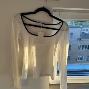 Vit ribbad långärmad topp från Mango - Storlek S. Helt ny inte använd. Säljer en vit ribbad långärmad topp från Mango med svarta kanter vid halsringningen. Toppen har en snygg, något djupare urringning och är i stretchigt material. Perfekt att styla till jeans eller kjol.