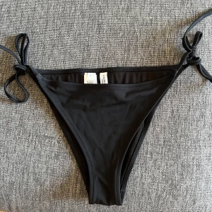 Svart bikiniunderdel från Calvin Klein - Svart OANVÄND bikiniunderdel från Calvin Klein med knyt i sidorna och tydlig logga framtill. Snygg och enkel design som passar till alla olika typer av överdelar.