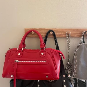 Röd handväska med silverdetaljer - Säljer en snygg röd handväska med silverfärgade detaljer och dragkedja framtill. Väskan har två handtag och en stilren design som passar perfekt till att lyfta vilken outfit som helst. Pris kan diskuteras vid snabb affär ❤️