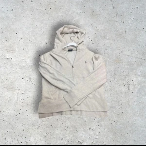 Grå hoodie från Polo Ralph Lauren - Säljer en beige hoodie från Polo Ralph Lauren med dragkedja framtill och klassisk broderad logga på bröstet. Tröjan har huva och fickor på sidorna, perfekt för en avslappnad stil.