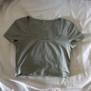 Olivgrön croppad t-shirt från H&M - Säljer en olivgrön croppad t-shirt från H&M med rund halsringning och korta ärmar. Tränings tröja i mjuk bomull