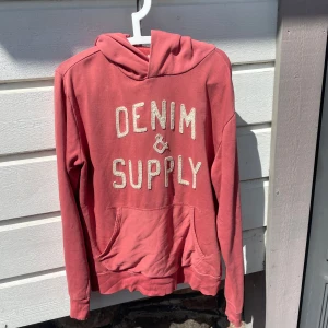 hoodie från Denim & Supply Ralph Lauren - Säljer en rosa hoodie från Denim & Supply Ralph Lauren med broderad vit text framtill. Tröjan har huva och en stor magficka. Perfekt för dig som gillar en avslappnad stil.