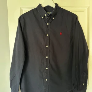Mörkblå skjorta från Ralph Lauren - Mörkblå ralph lauren skjorta. Använd fåtal gånger därav väldigt fint skick. Hör av dig vid minsta fundering!