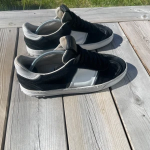 Valentino flycrew  - Säljer ett par snygga svarta och vita sneakers från Valentino. Skorna har svart mocka och vita skinnpaneler, samt vit sula. Klassisk rund tå och platt sula. Perfekta för dig som gillar stilrena och exklusiva sneakers. Finns inte nya. Storlek 40 med 5 nitar borta. Skriv vid alla frågor!