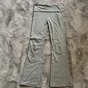 Grå bootcut byxor från Gina Tricot - Gråa mjuka byxor från Gina Tricot med bootcut-ben och övervikt midja.  Byxorna är i stretchigt material och har en enkel, stilren design utan synliga detaljer. Perfekta för en avslappnad och trendig look.