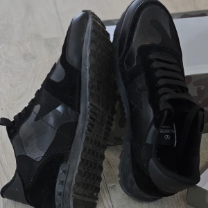 Svarta Valentino Rockrunner sneakers/ 43 - Säljer ett par svarta Valentino Rockrunner sneakers med kamouflagemönster och svarta detaljer. Skorna har endast använts en gång men eftersom de va för stora säljer jag de Kommer i kartong med röd dustbag och extra skosnören. OBS! Priset kan diskuteras och sänkas vid snabb och smidig affär