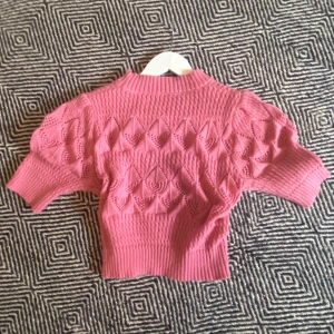Oanvänd rosa  stickad topp med mönster  - Säljer en rosa stickad topp med korta ärmar och snyggt hålmönster i diamantform. Tröjan har ribbade muddar vid hals, ärmslut och nederkant. Aldrig använd. (Nypris:150kr)