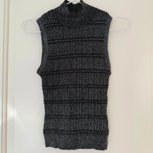 Svart och silvrig topp från Esprit - Säljer en svart och silvrig topp från Esprit. Perfekt att styla över en skjorta eller långärmad tröja för en trendig lager-på-lager-look. Tight passform.