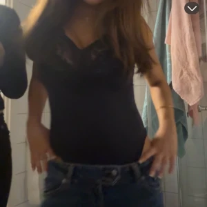 Svart spetslinne med v-ringning - Säljer ett svart linne med v-ringning och spetsdetaljer upptill. Sitter tight och har tunna axelband. Perfekt att styla med jeans eller kjol för en trendig look.