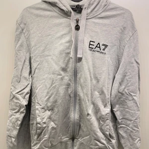 EA7 Kofta - Ljusgrå hoodie från EA7 Emporio Armani, hade behövts strykas om man inte gillar skrynkliga kläder, syns inte lika mycket när man har den på sig som på bilden. Alla prisförslag är välkomna vill bara få bort från min garderob 