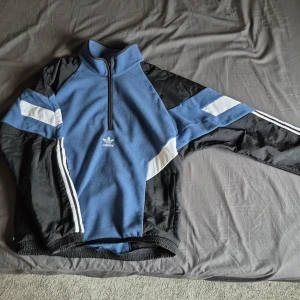 Blå och svart fleece-tröja från Adidas - Säljer en half zip fleece-tröja från Adidas. Den är storlek S men passar mig som alltid bär M väldigt bra. Tröjan är inte använd så mycket så den är i väldigt gott skick. Nypris är omkring 1000 kr men tror inte den säljs längre. Pris kan absolut diskuteras.