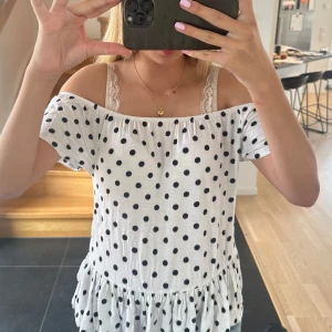 Vit prickig offshoulder blus - Supersöt vit blus med svarta prickar och offshoulder-modell. Toppen har korta ärmar och volang nertill som ger en extra gullig vibe. Perfekt till jeans eller kjol! Köptes på Vinted!