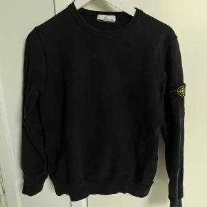 Svart sweatshirt från Stone Island - Svart sweatshirt från Stone Island med klassisk rund hals och ribbade muddar. Tröjan har den ikoniska Stone Island-patchen på vänster ärm. Tillverkad i mjuk bomull, perfekt för dig som gillar stilrena och enkla plagg med streetkänsla. Säljer den pga att den är för liten tyvärr. Köpt från NK, fick den i julklapp. Skicket är bra inte fläckar eller defekter men den har användts. Storleken är xs men jag skulle säga att den passar s också😁🤩