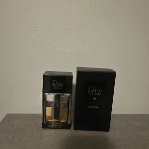 Dior Homme Intense Eau de Parfum - Dior Homme Intense är en lyxig herrparfym med elegant svart förpackning och stilren glasflaska. Doften är varm och sofistikerad, perfekt för dig som gillar exklusiva och maskulina toner. Flaskan har en svart detalj i mitten och guldtonad vätska cirka 30 ml kvar.