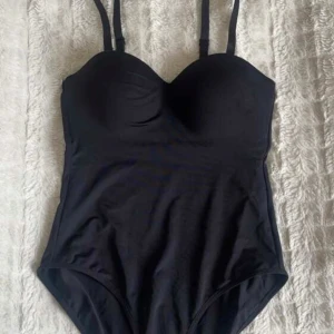 Svart body med bygel och axelband - Snygg svart body med formpressade kupor och bygel för extra stöd. Axelbanden är justerbara samt går att ta bort och modellen har en klassisk, stilren look. Materialet är mjukt och formar kroppen fint 😍 perfekt till att klä upp eller ner! I storlek xs