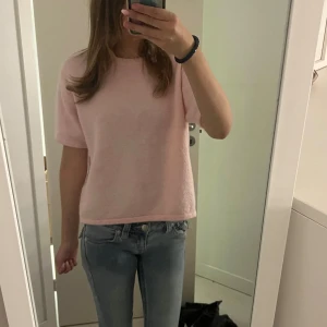 Ljusrosa stickad topp med kort ärm - Superfin ljusrosa stickad topp med korta ärmar och rund hals. Modellen är rak och lite boxig, vilket ger en avslappnad vibe. Perfekt att matcha med jeans eller kjol för en söt och enkel look.