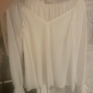 Vit blus med volang - Superfin vit blus med långa ärmar. Blusen har volangdetaljer längs ärmarna och en luftig, flowy passform. Perfekt för dig som gillar romantisk och stilren look.