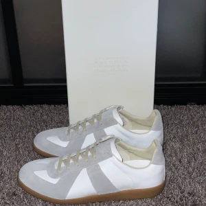 Maison Margiela sneakers vit/grå - Maison Margiela sneakers i vitt och ljusgrått med ovandel i skinn och mocka och klassisk gummisula. Perfekta för dig som gillar stilrena och trendiga sneakers. Storlek 42 men passar också 41. Priser är ej hugget i sten, skriv gärna vid minsta lilla fundering! 