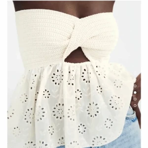 Vit bandeau tubtopp med broderi - Supersöt vit bandeau tubtopp med twistad överdel i virkad look och broderad, utsvängd nederdel med blommiga hålmönster. Toppen är axelbandslös och har en liten cut-out framtill. Perfekt för varma dagar och ger en romantisk vibe. Från zara
